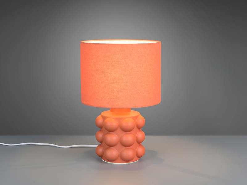 Orangene Retro-Tischleuchte mit kugelförmig strukturiertem Keramikfuß und Stoffschirm angeschaltet