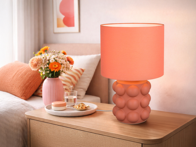 große orangene Tischleuchte mit Keramikfuß und Stoffschirm auf einer Kommode