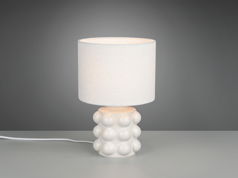 Weiße Retro-Tischleuchte mit kugelförmig strukturiertem Keramikfuß und Stoffschirm angeschaltet