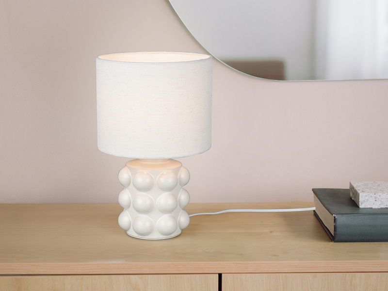Weiße Tischleuchte mit kugelförmig strukturiertem Keramikfuß und Stoffschirm auf einer Kommode