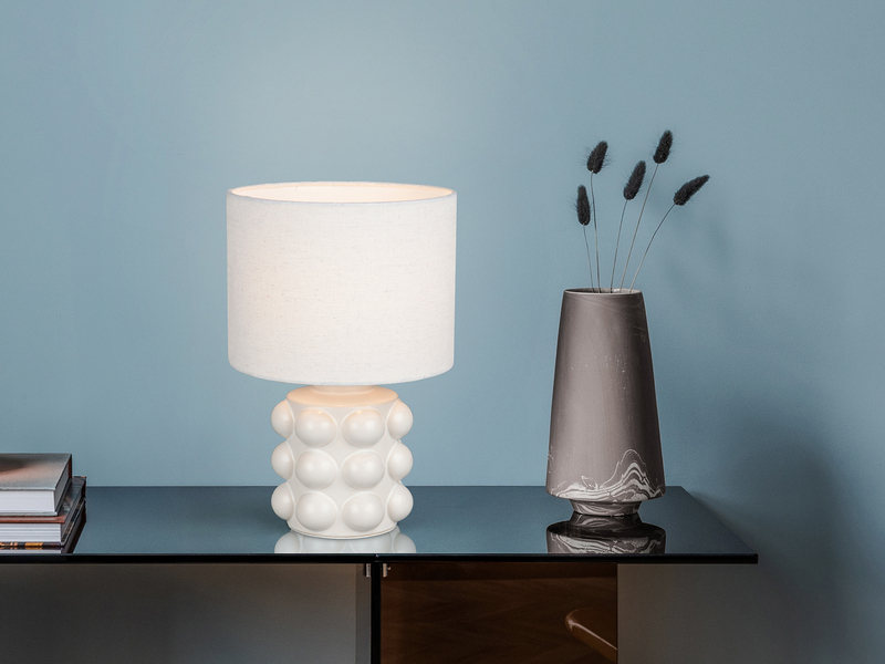 Weiße Tischleuchte mit Keramikfuß und Stoffschirm auf einer Kommode
