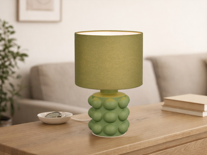 Grüne Tischleuchte mit Keramikfuß und Stoffschirm auf einer Kommode
