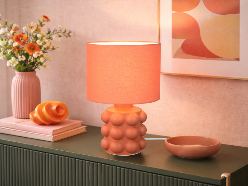 Orangene Tischleuchte mit Keramikfuß und Stoffschirm auf einer Kommode