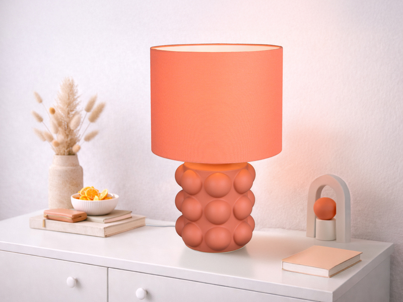 große orangene Tischleuchte mit Keramikfuß und Stoffschirm auf einer Kommode