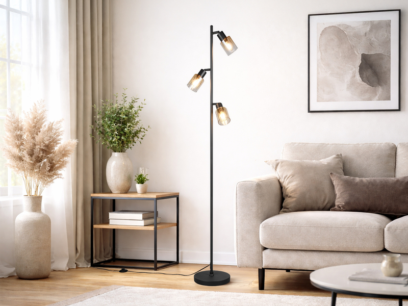 Stehlampe mit schwarzem Fuß und drei amberfarbigen Glas Spots in einem Wohnzimmer neben dem Sofa stehend